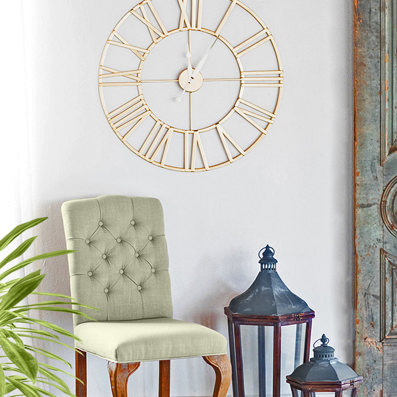 Anya, gold tone, minimalist round wall clock featuring Roman numerals - in living room setting with chair, lamps, and door decor