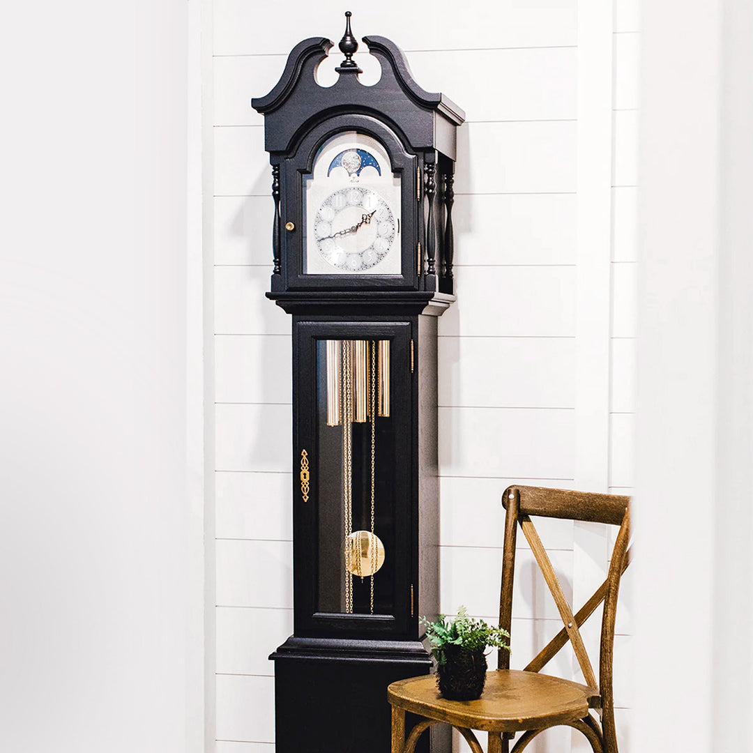 Black grandfather clock with pendulum against a white wall.