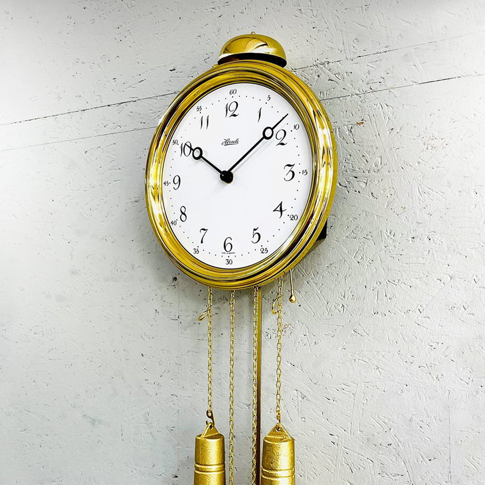 Gold wall clock with pendulum on a textured white wall