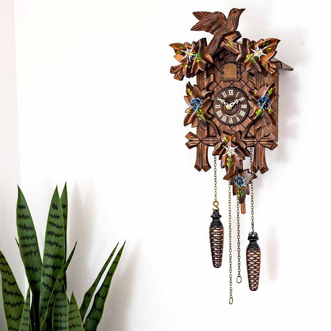 Wooden cuckoo clock with decorative elements on a white background above potted plant