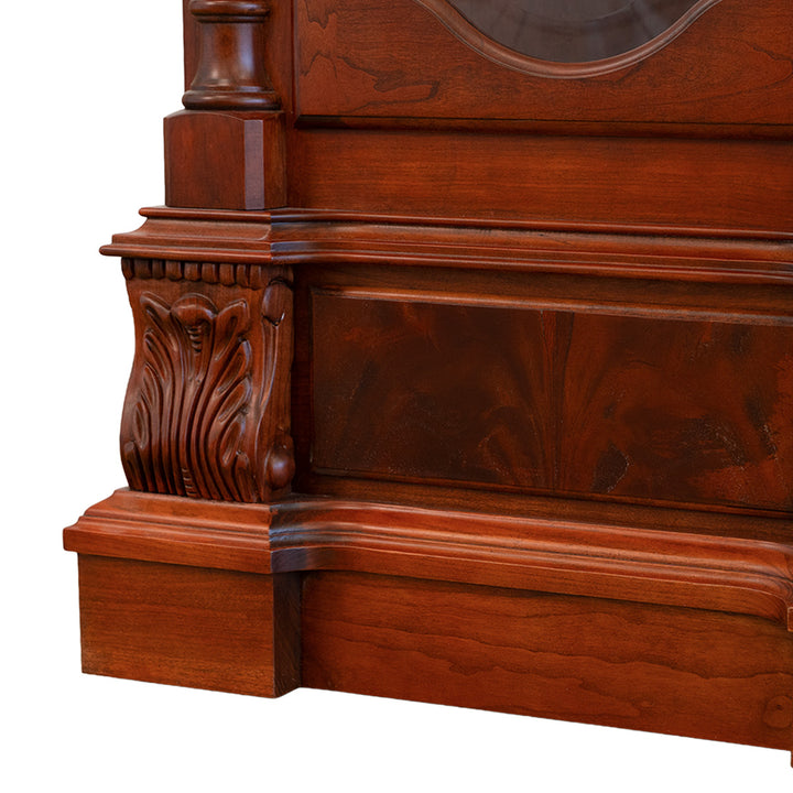 Close-up of grandfather clock base made of detailed carved cherry wood on white background.