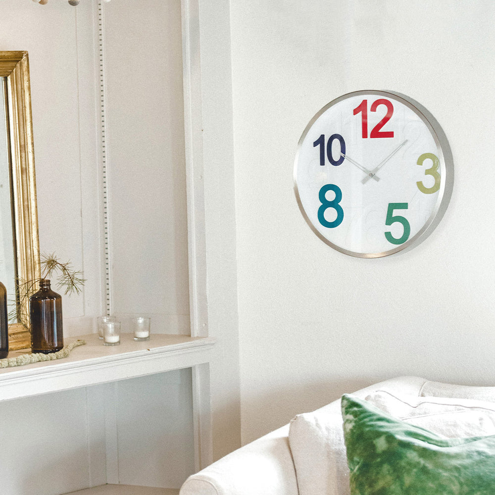 Wall clock with colorful numbers hanging on white wall next to shelf with candles in living room.