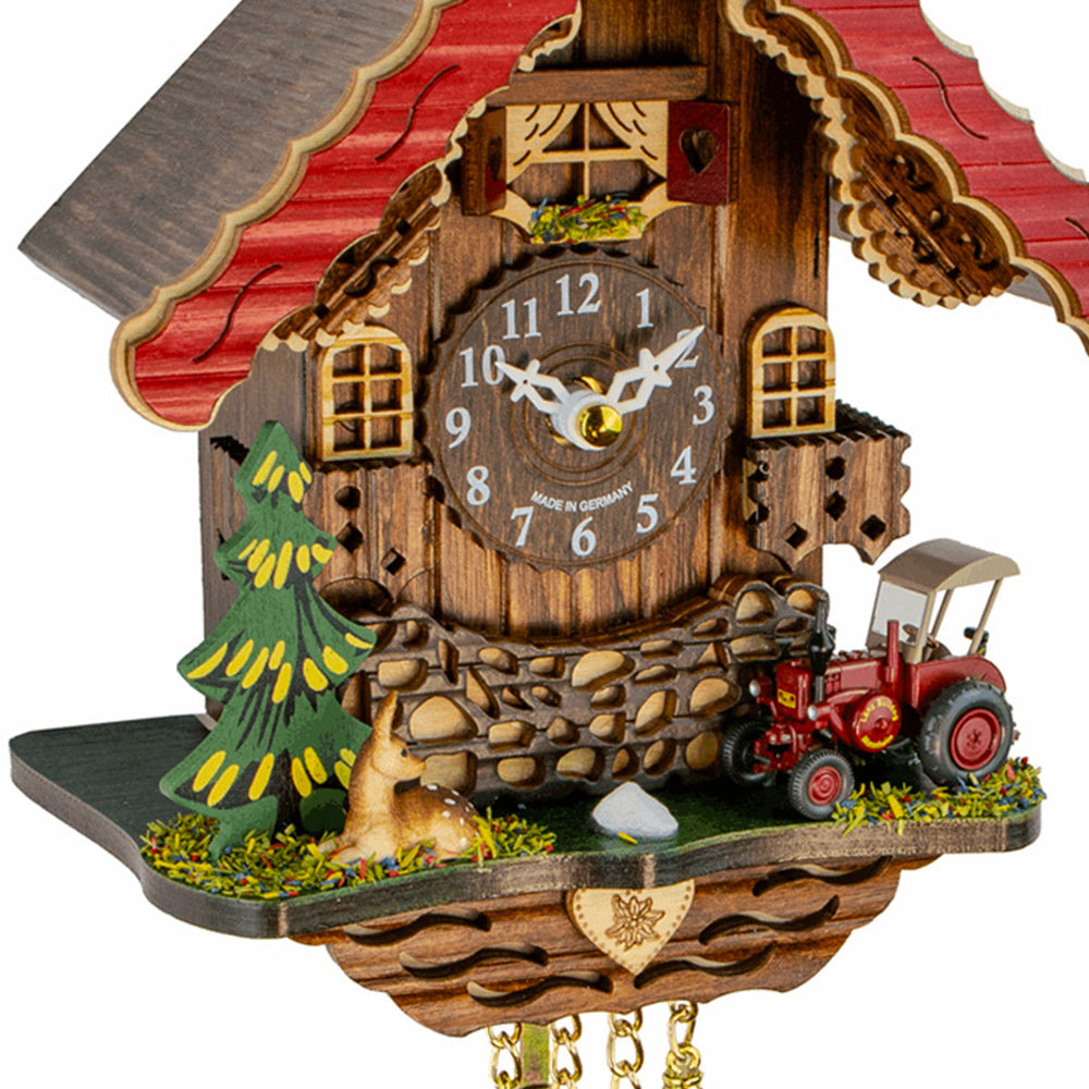 Close-up of red trimmed wooden cuckoo clock with red tractor on white background.