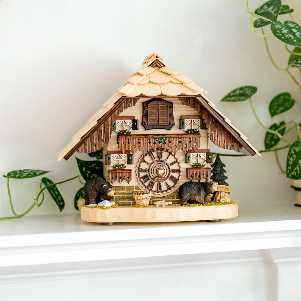 Wooden cuckoo clock with bear figures and painted flowers on white shelf with green plant nearby.