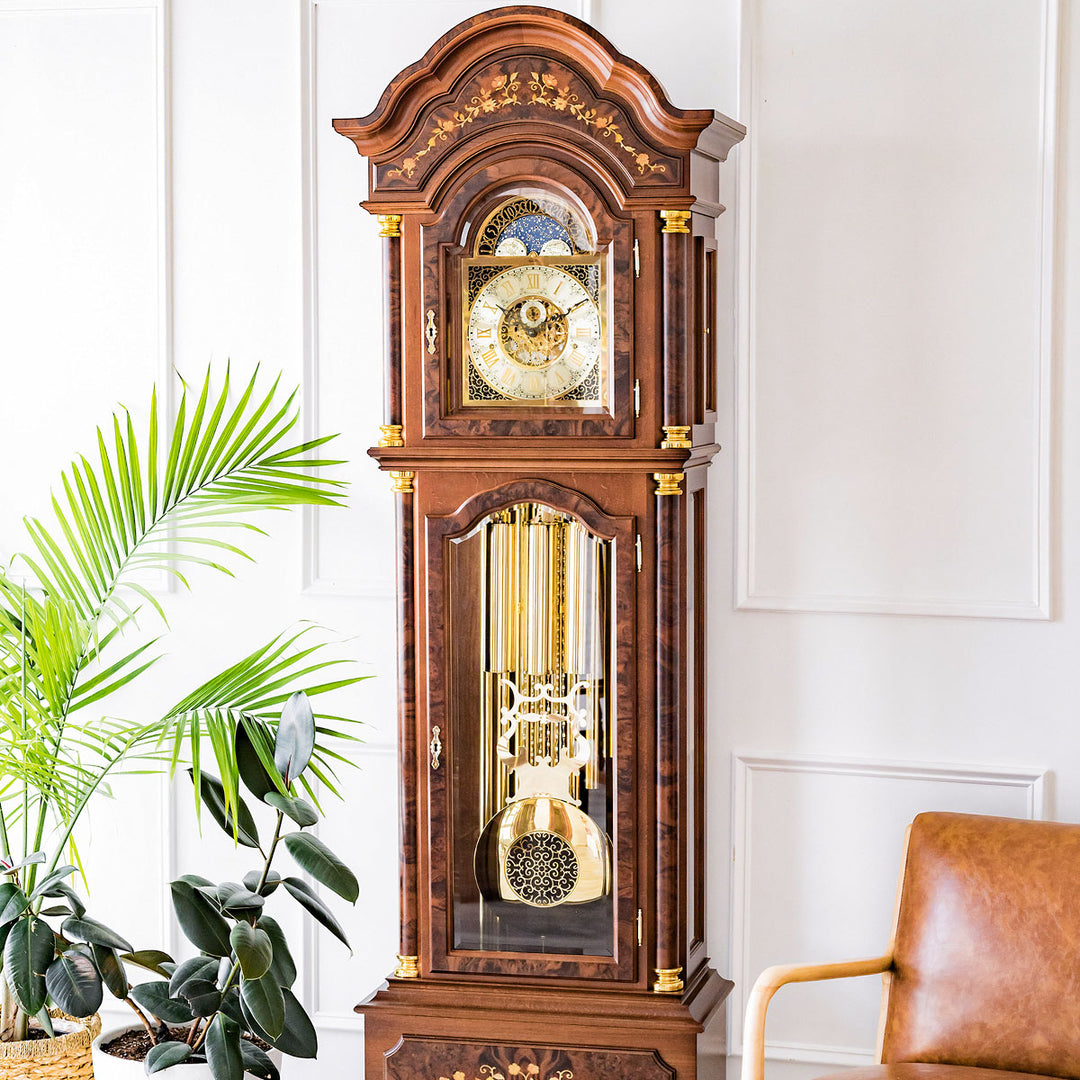 Wooden grandfather clock with brass weights and pendulum in white room next to green plant and leather chair 