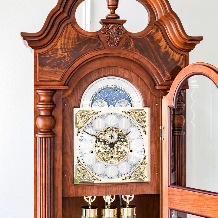 Ornate wooden grandfather clock with detailed brass face and moon dial against white wall