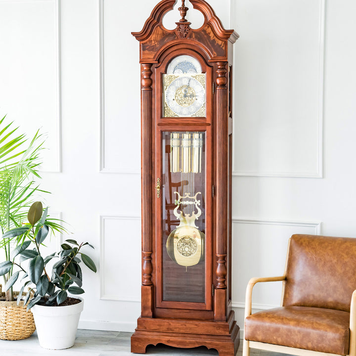 Cherry wood grandfather clock in a room with a plant and brown leather chair.