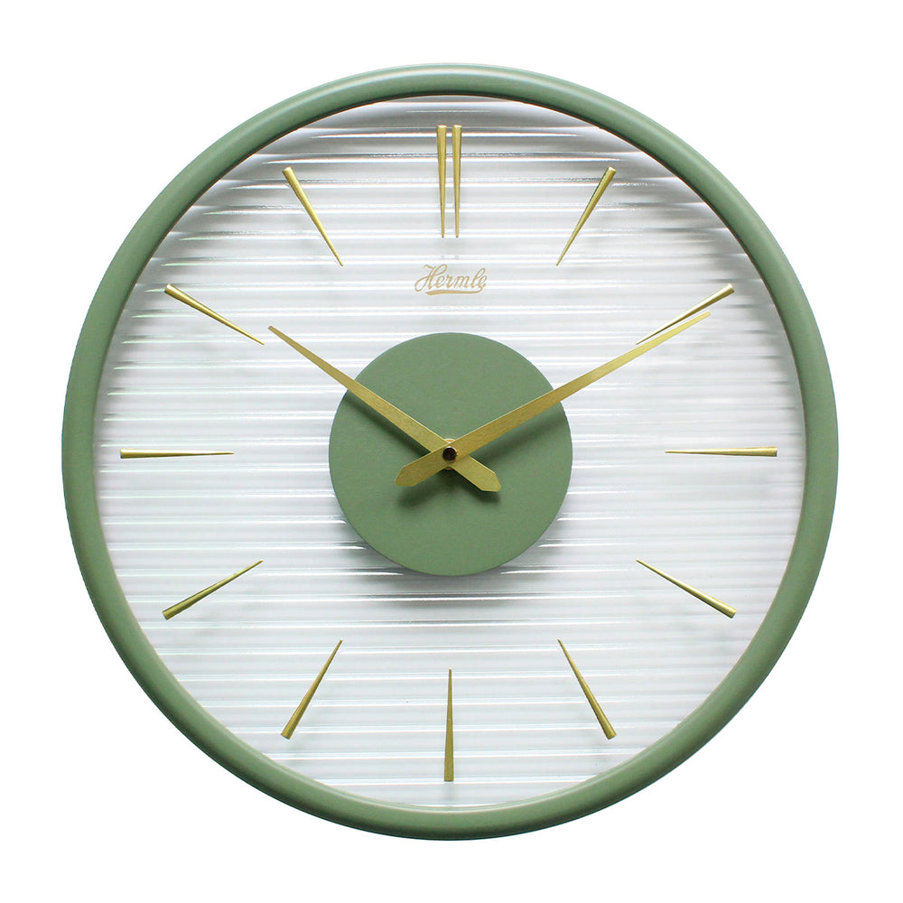 Green wall clock with gold numeral markings and clear ridged plastic face on white background.