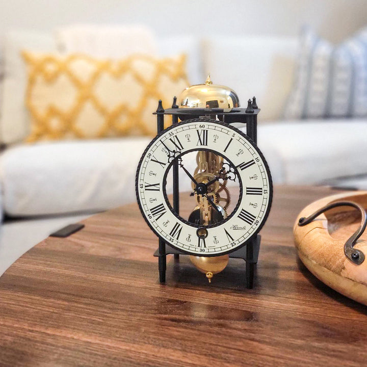 Decorative black mantel clock with brass gears on wooden coffee table.