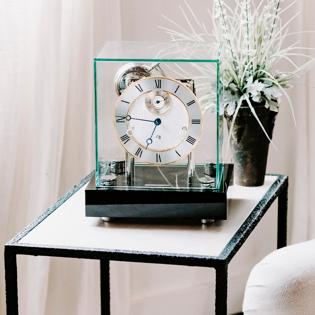 Black desk clock with glass cube cover sitting on black and white side table in white room 