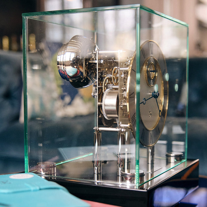 Intricate nickel gears inside glass case of black desk clock 