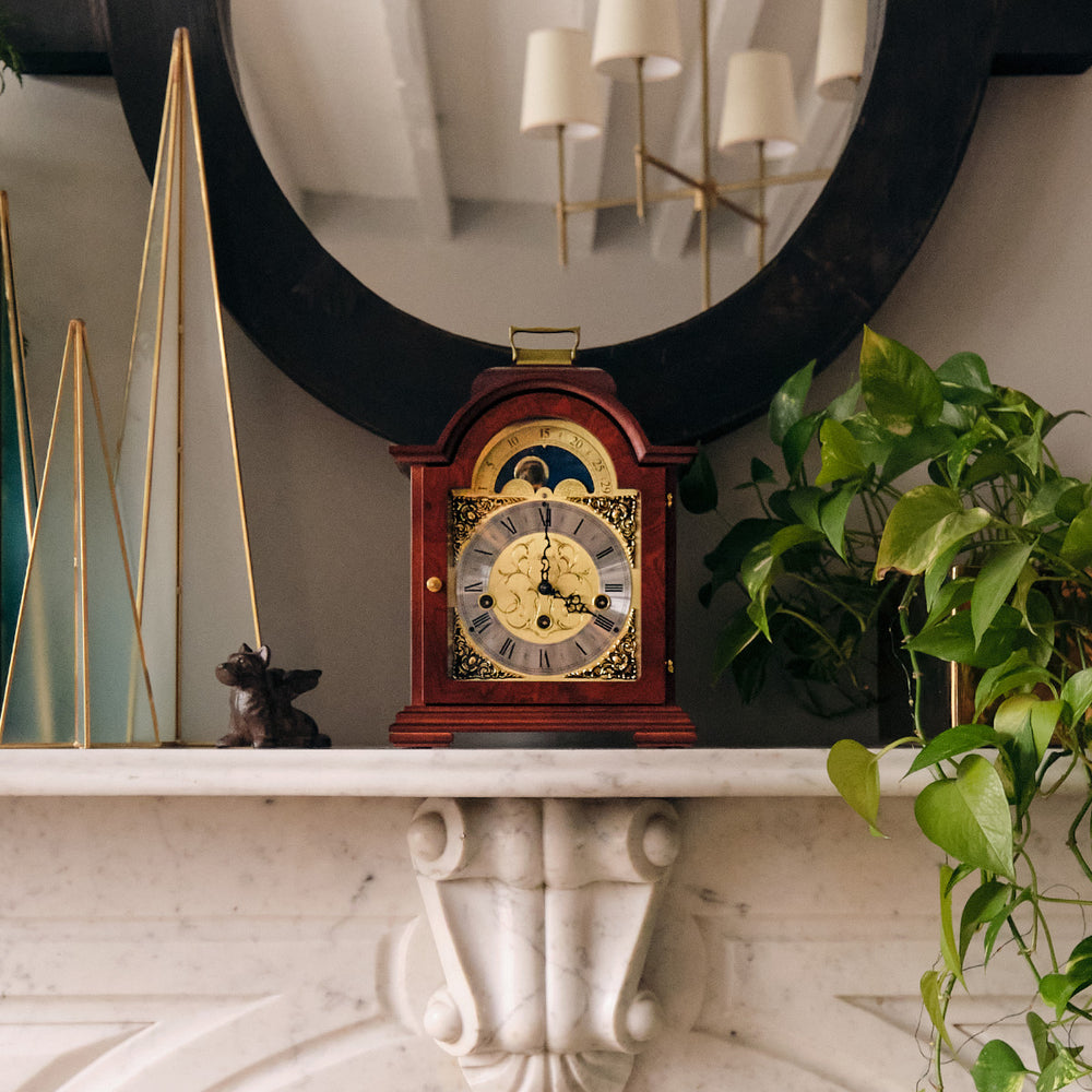 Mahogany and brass clock on white marble shelf surrounded by decorative plants