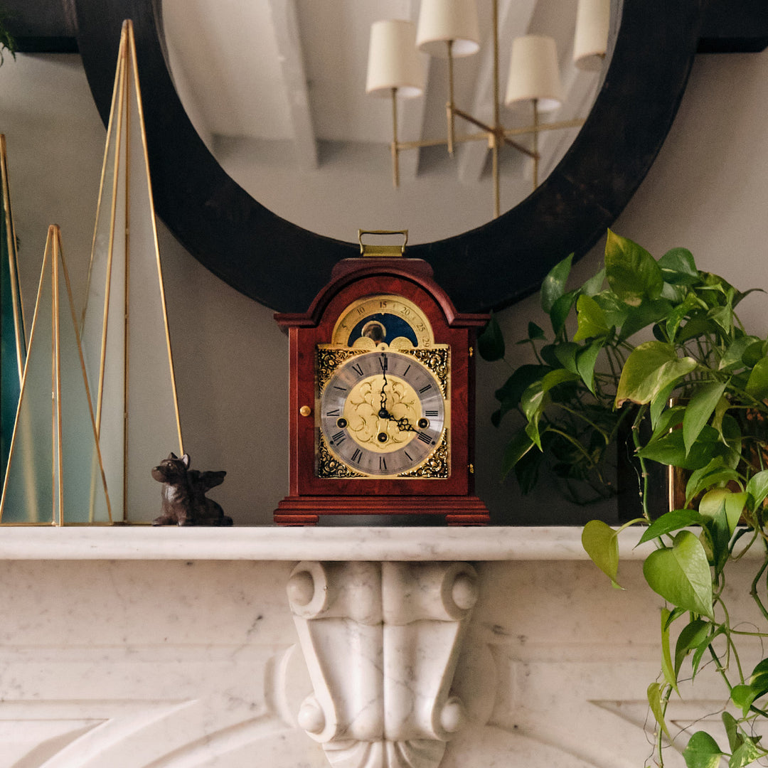 Mahogany and brass clock on white marble shelf surrounded by decorative plants