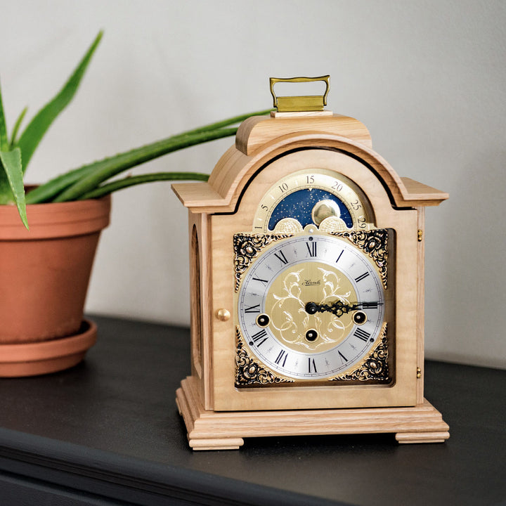 Light oak clock on black mantle with decorative plant 
