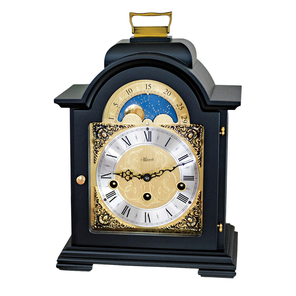 Black and brass mantel clock with roman numerals, ornate face and moon dial on white background.