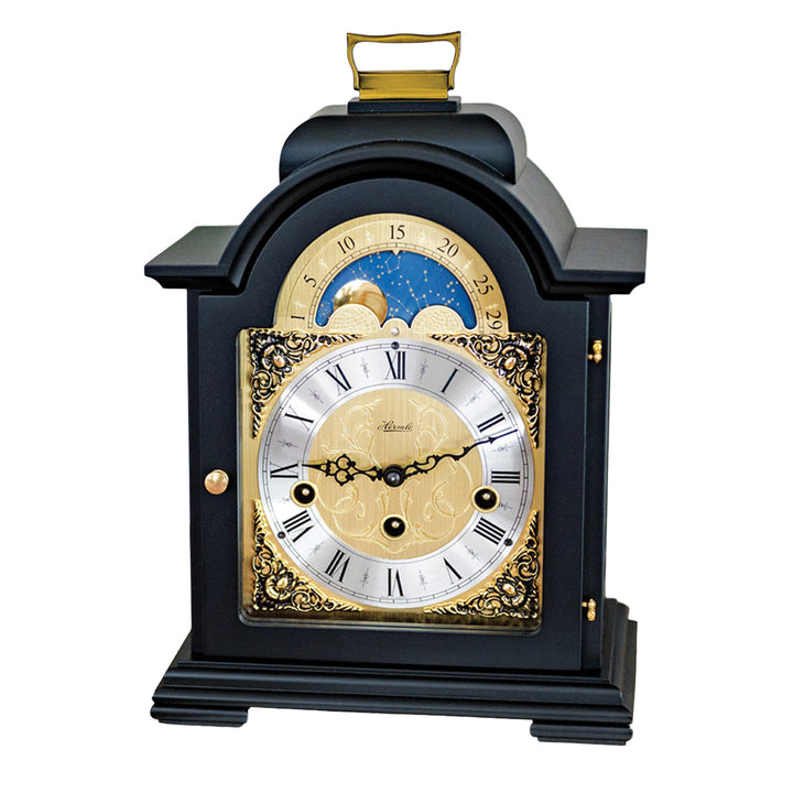 Black and brass mantel clock with roman numerals, ornate face and moon dial on white background.