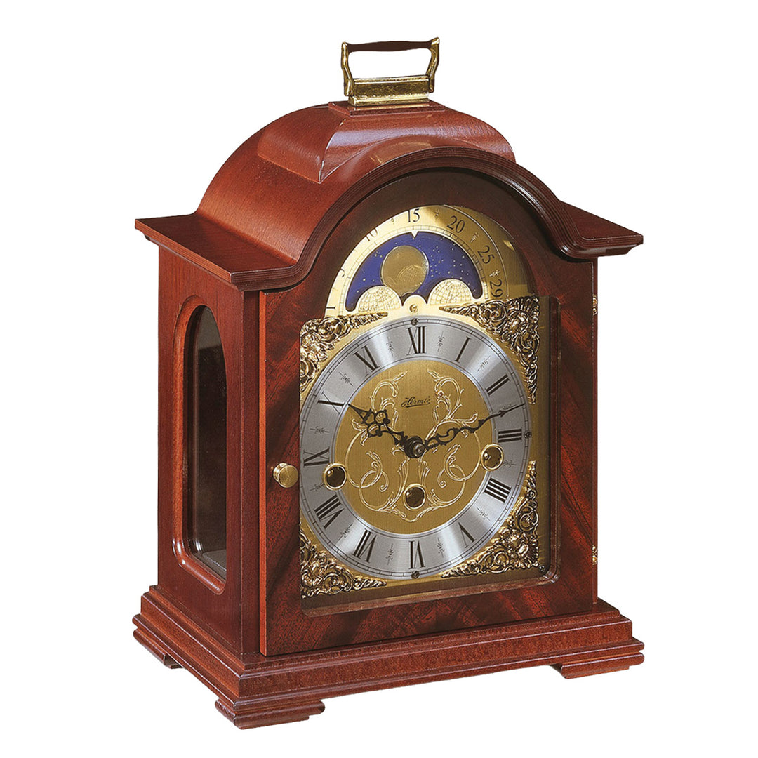 Mahogany wood and brass mantel clock with roman numerals, ornate face and moon dial on white background.