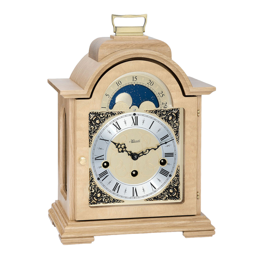 Oak wood and brass mantel clock with roman numerals, ornate face and moon dial on white background.