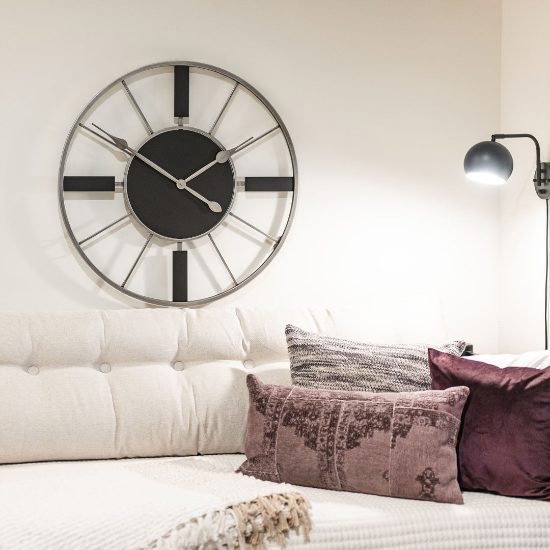 Black and metal wall clock hanging above white couch in living room.