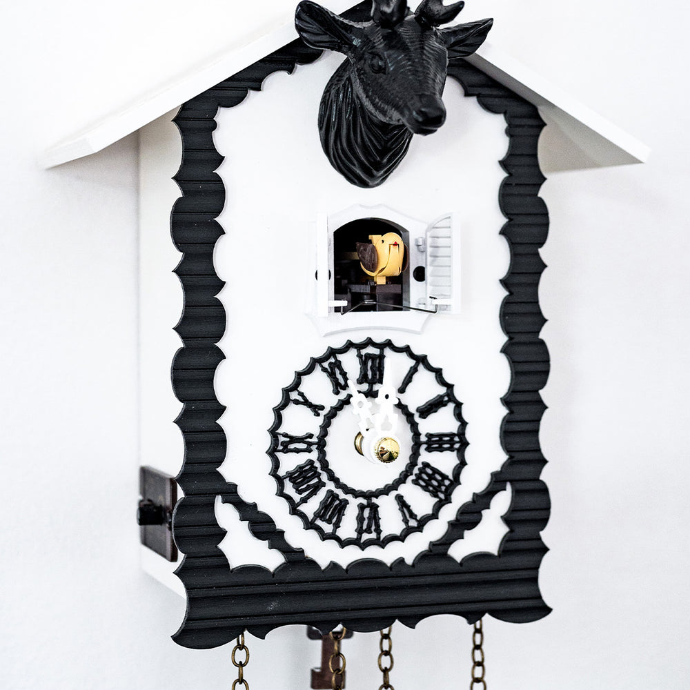 Up close of black and white cuckoo clock with cuckoo bird coming out of door and roman numeral face