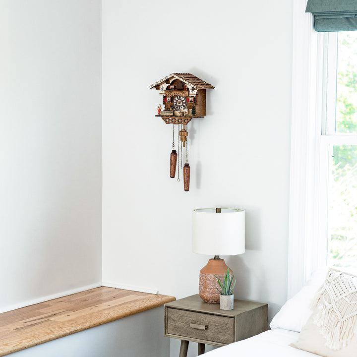Wooden German cuckoo clock hanging in white room above wooden nightstand with lamp