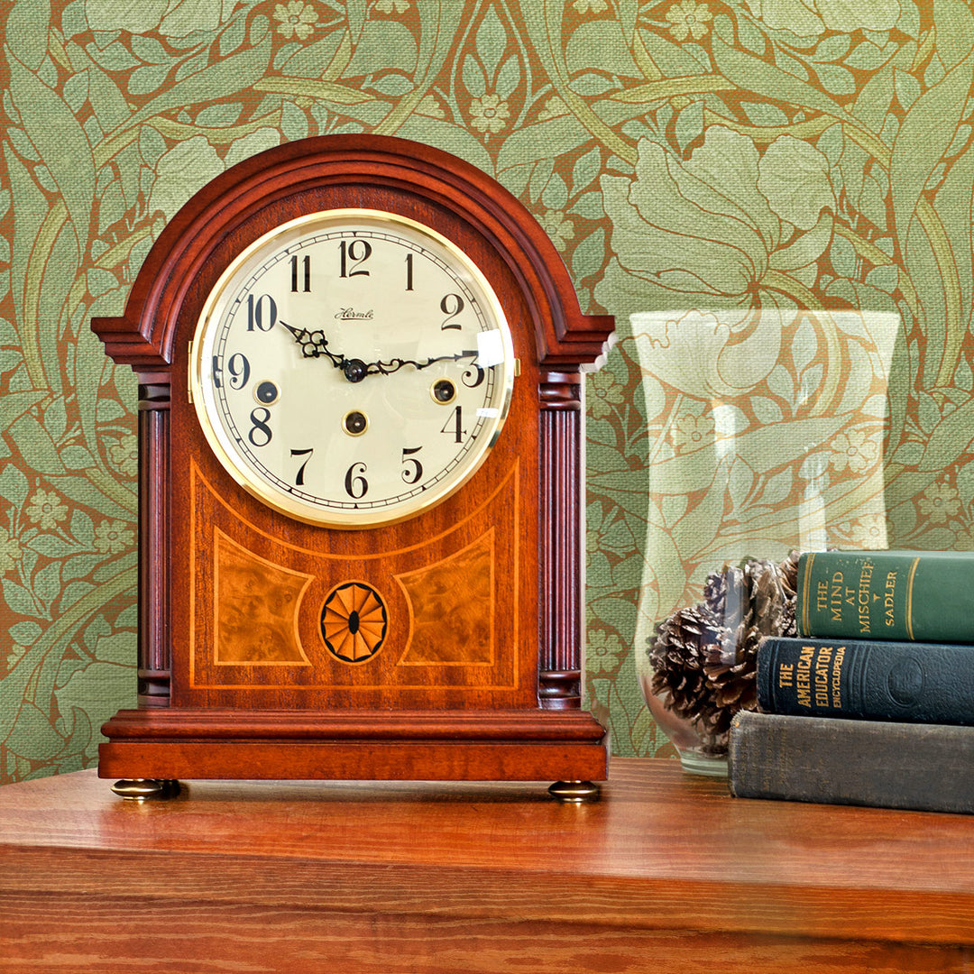 Wooden mantel clock on a wooden cabinet with decorative William Morris wallpaper in the background