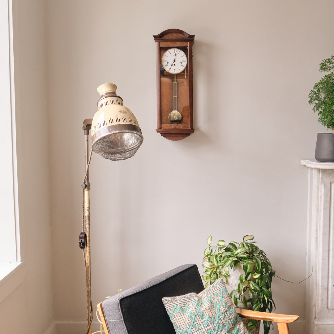 Wooden wall clock hanging on living room wall above chair decorative plants