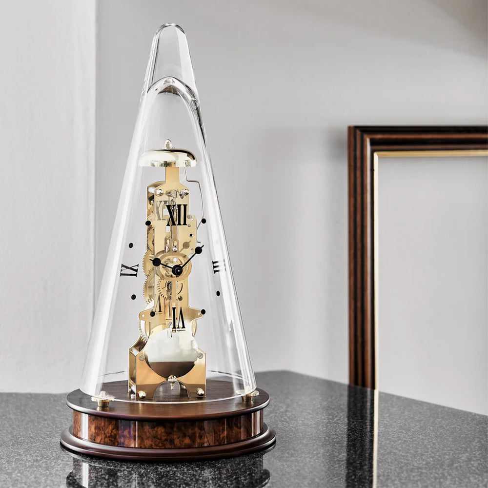Decorative mechanical clock under a glass dome on a marble countertop with a white wall in the background