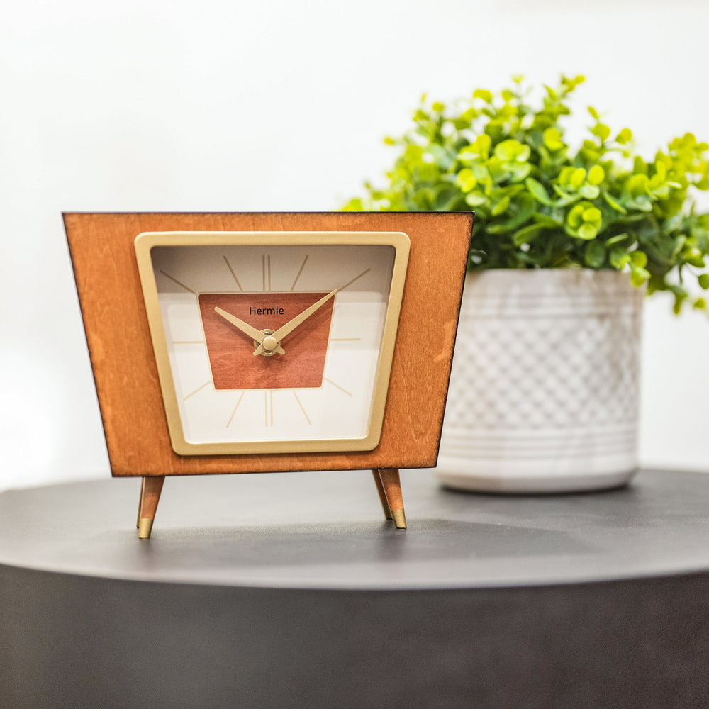 Retro style desk clock on gray side table in front of green plant in white room.
