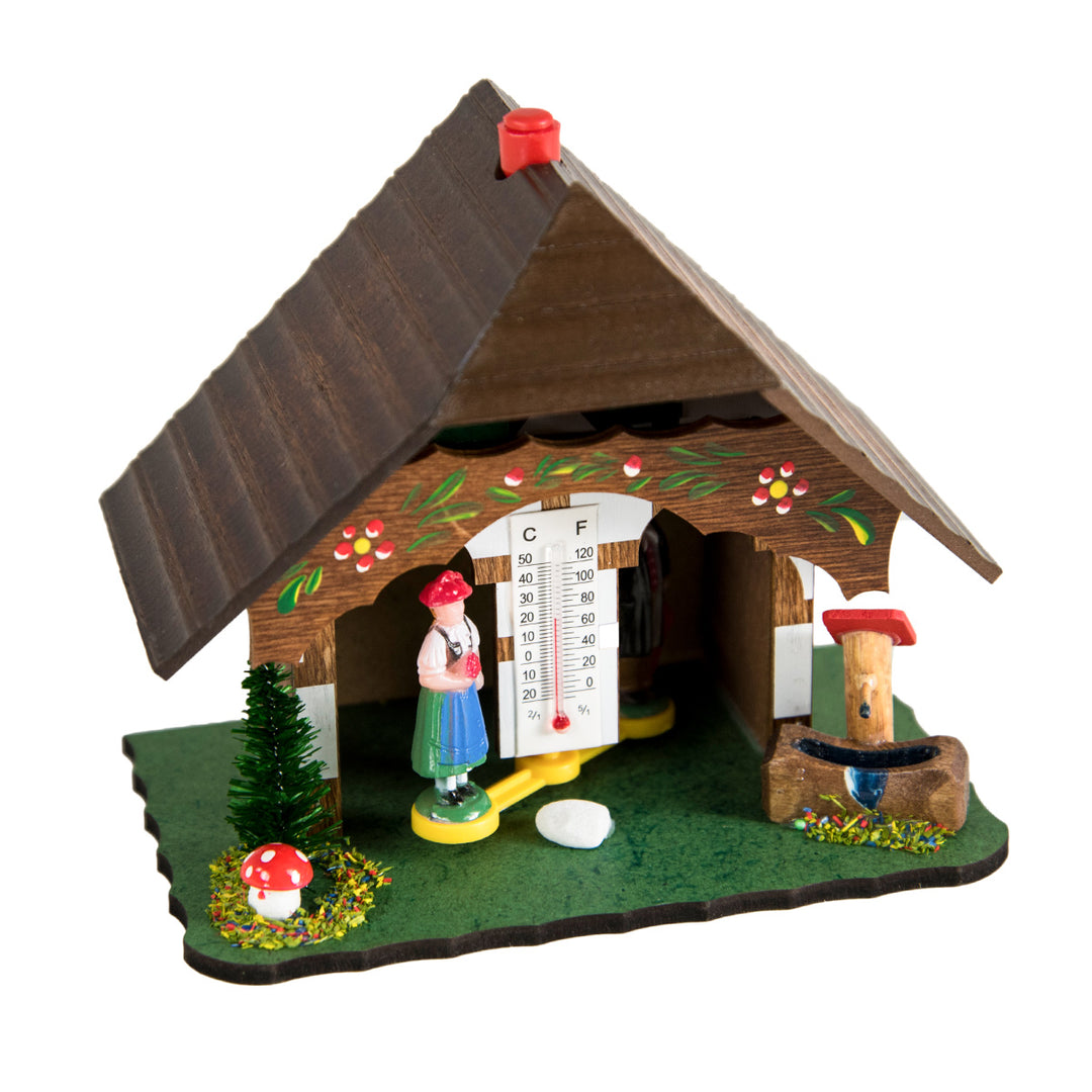 Wooden German style weather station with pine trees and man and woman figurines on white background.