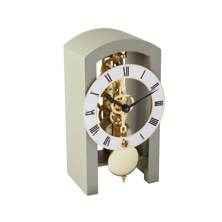 Mechanical clock with grey casing and silver face highlighted by brass on a white background