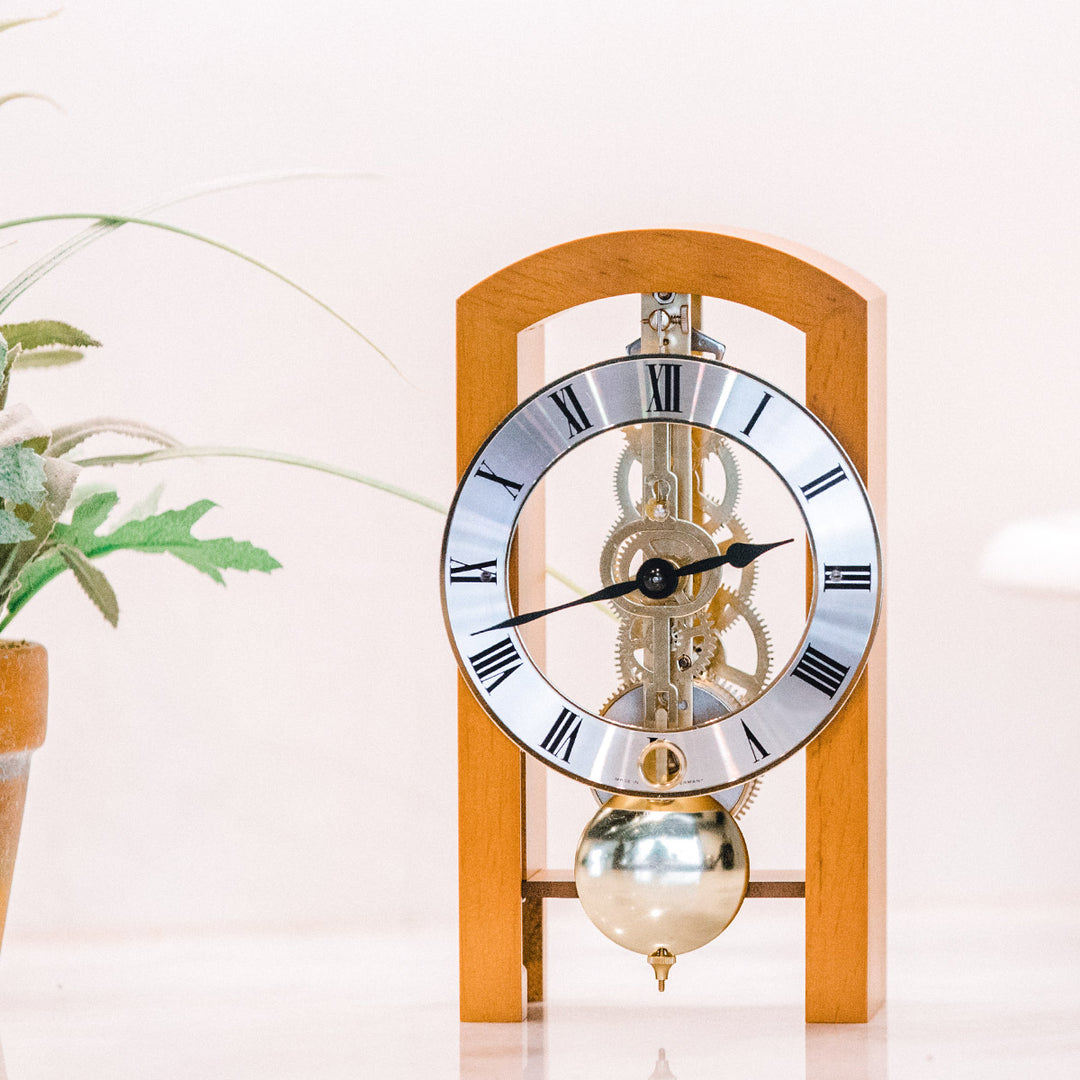 Light cherry mechanical clock on white table next to small plant