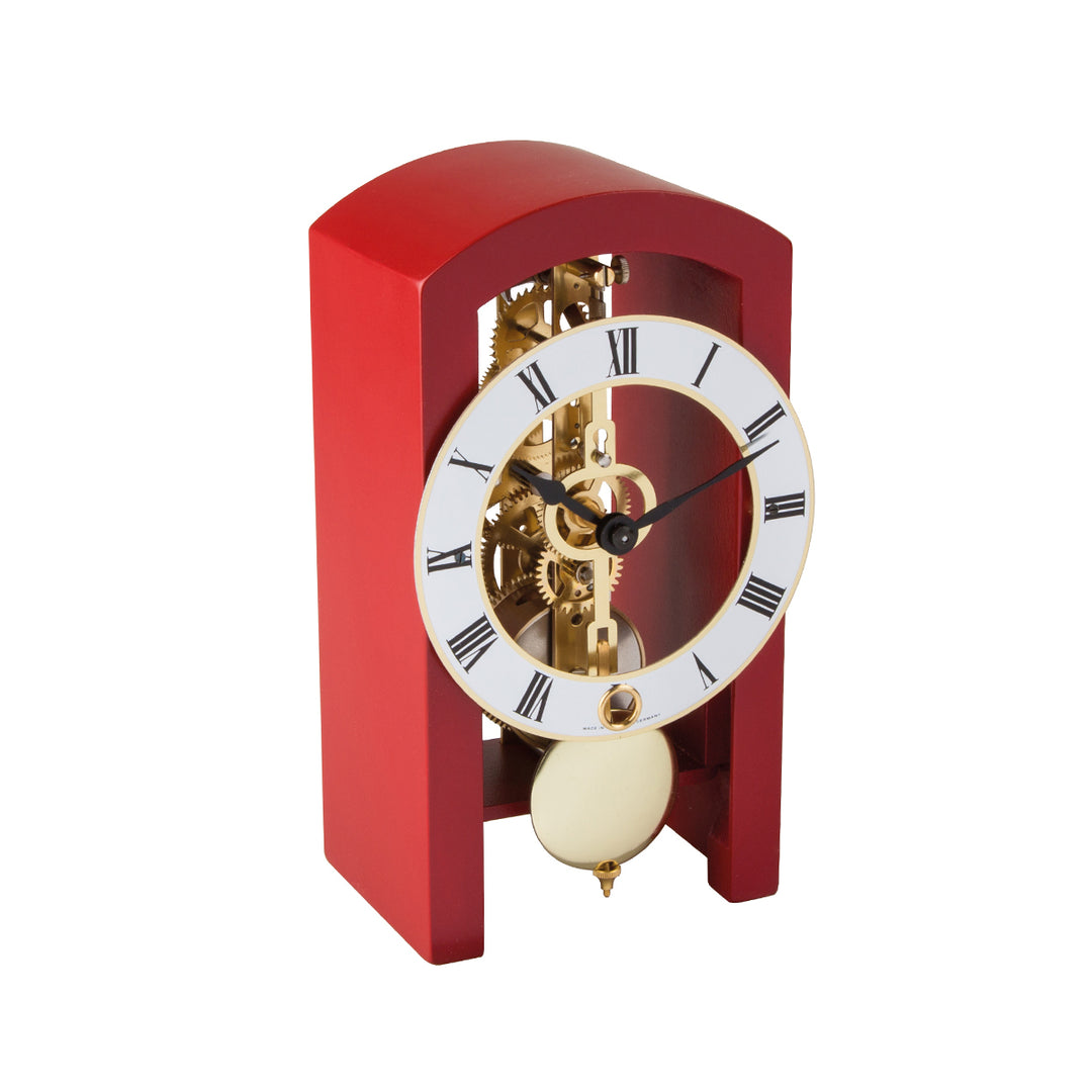 Mechanical clock with red casing and silver face highlighted by brass on a white background