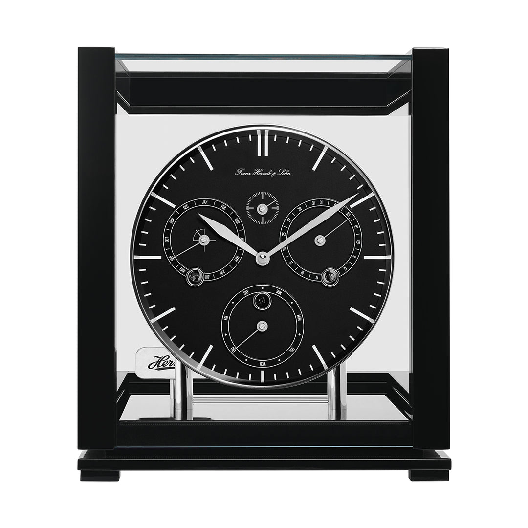 Front view of black perpetual calendar clock with black face, silver hands and glass panels on white background.