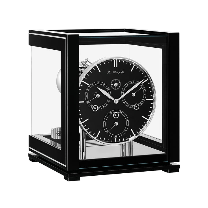 Black perpetual calendar clock with black face, silver hands and glass panels on white background.