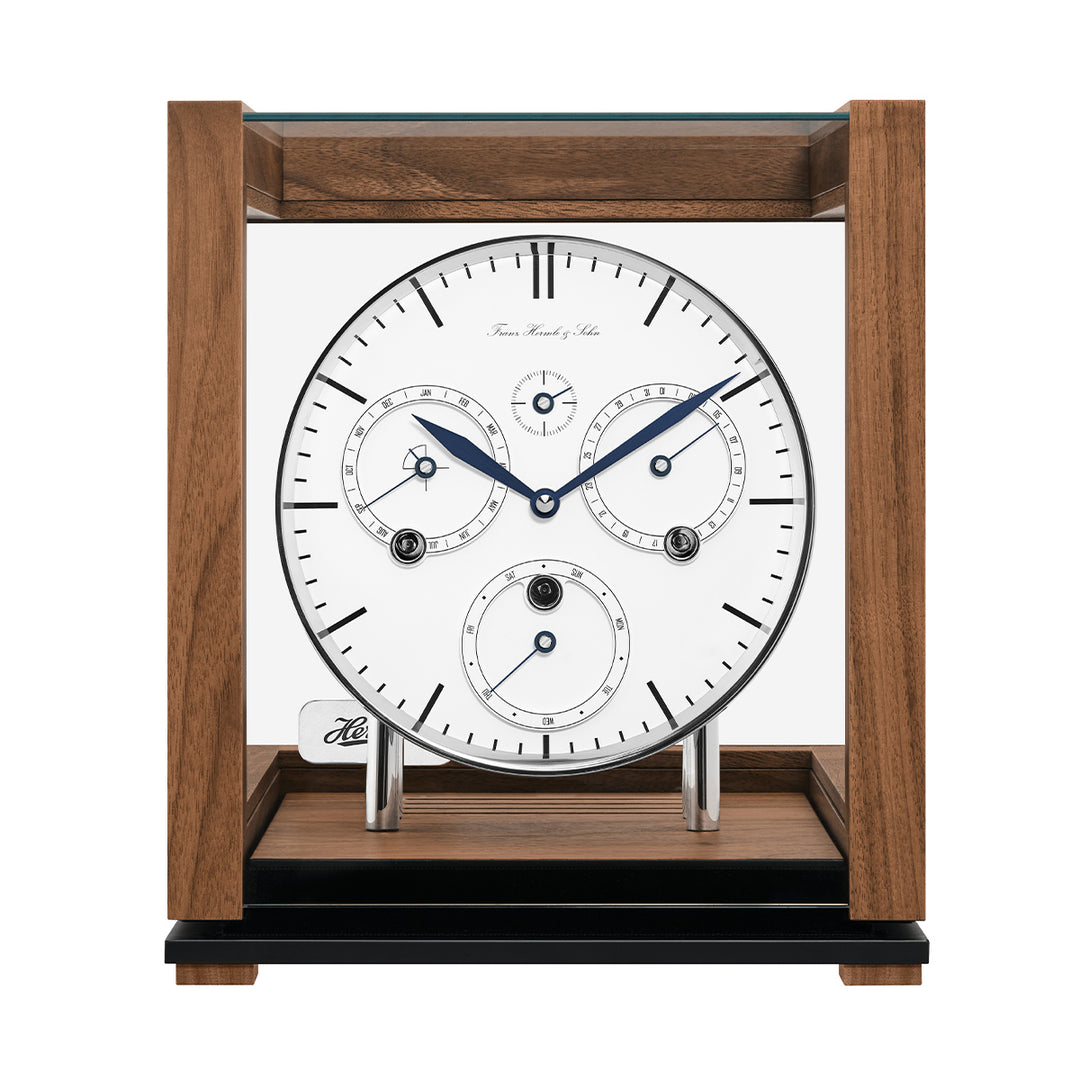 Front view of walnut perpetual calendar clock with blue hands and glass panels on white background.