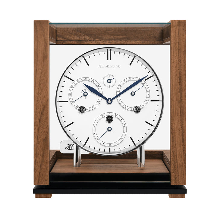 Front view of walnut perpetual calendar clock with blue hands and glass panels on white background.