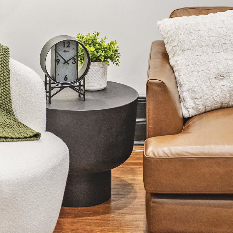 Living room with a black side table, small iron clock, and potted plant between two couches.
