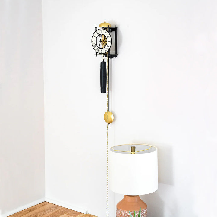 Black skeleton clock hanging on white wall above decorative lamp
