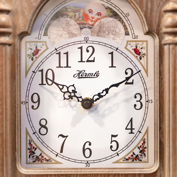Close up of illustrated clock face with moon dial and arabic numbers on wooden clock. 