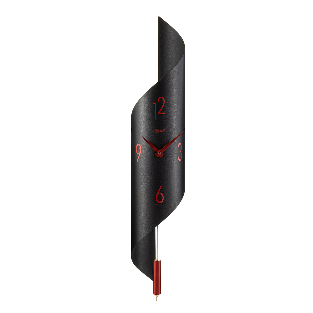 Black finish abstract clock with red finish pendulum and arabic numerals on white background.
