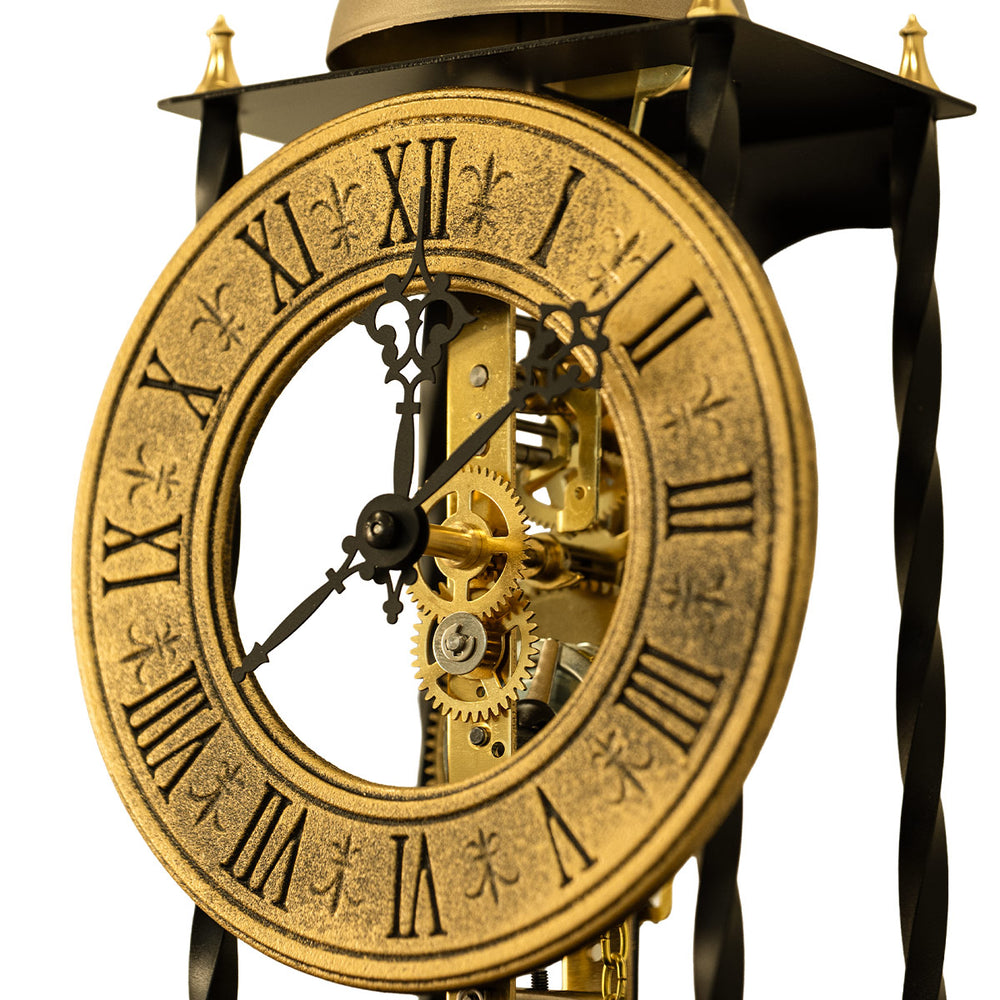 Close up of black antique-style brass clock face and gears on white background.