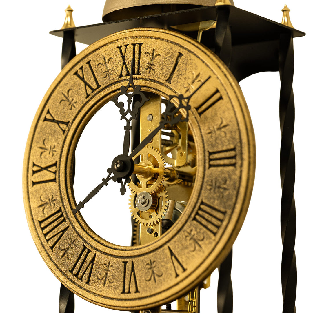 Close up of black antique-style brass clock face and gears on white background.