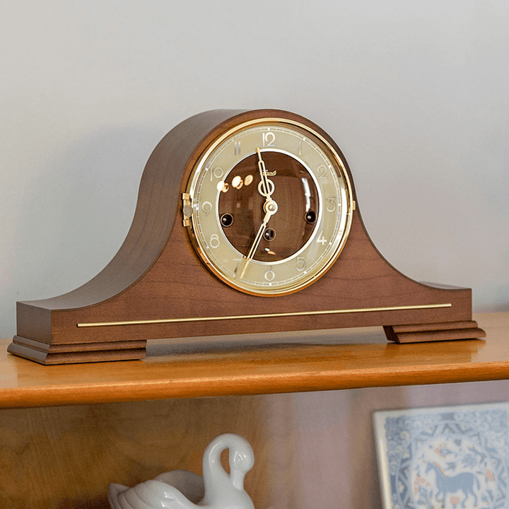 Wooden tambour style mantel clock with an off-white face on a wooden shelf. Clock is Stepney by Hermle in a mid-century modern style.