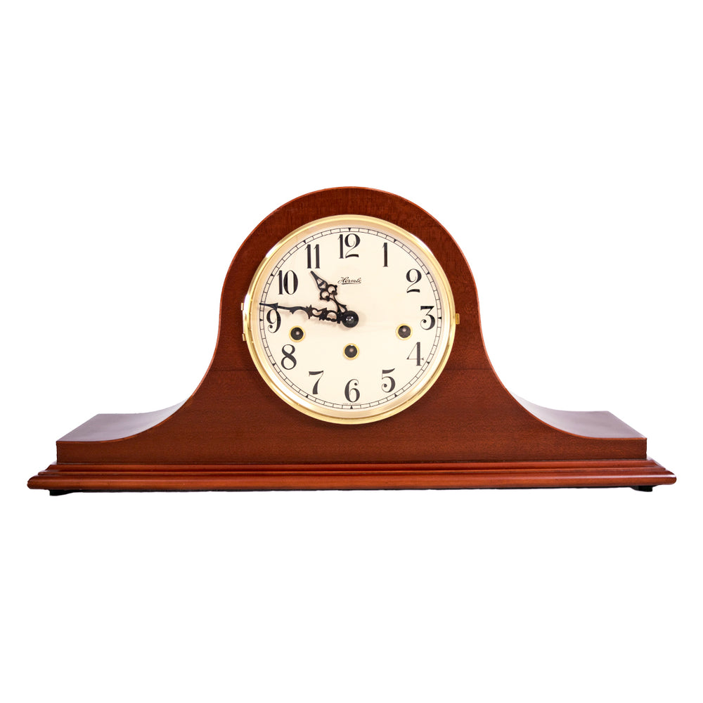 Wooden mantel clock with white face and holes for winding the mechanical movement on a white background.