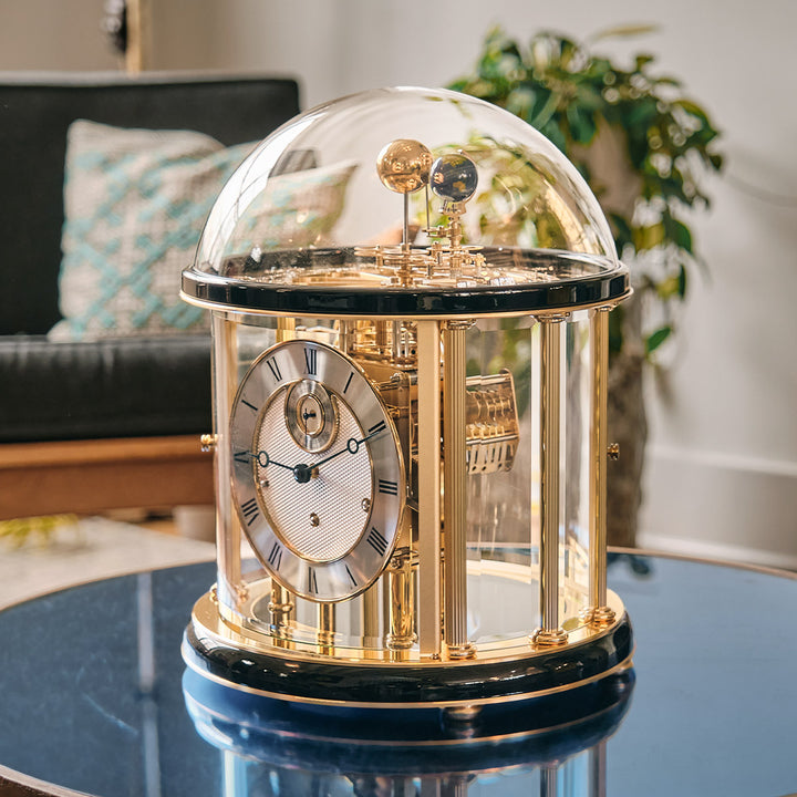 Decorative Tellurium clock with a clear dome and intricate gold gears on a table in a living room setting