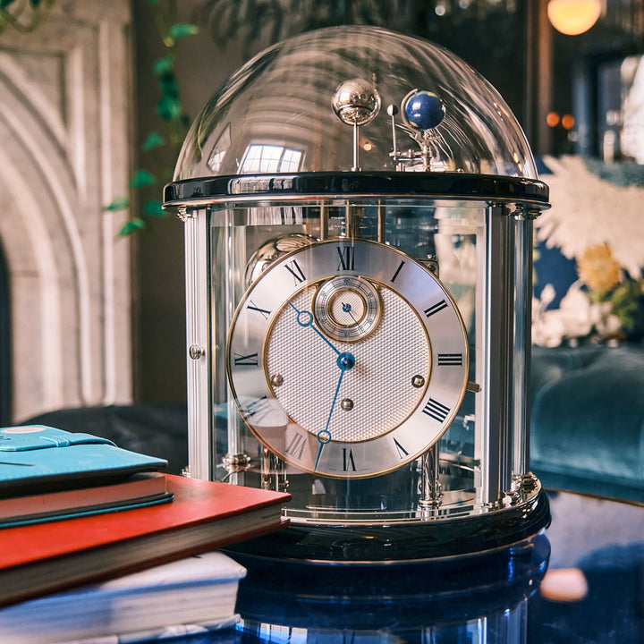 Black and nickel Tellurium clock with glass dome in living room on blue table.