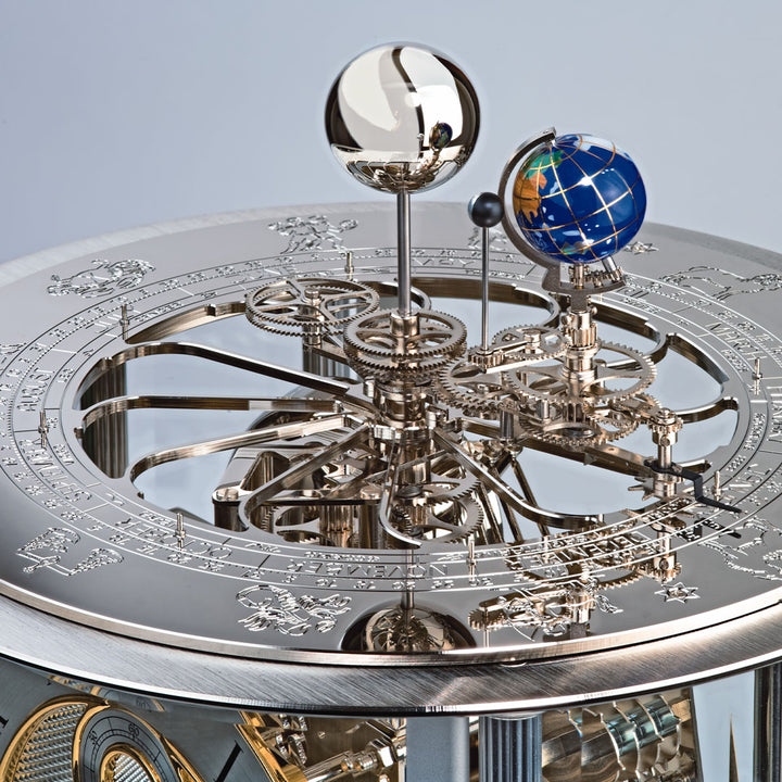 Close-up of a detailed mechanical clock with celestial globe on a light blue background.