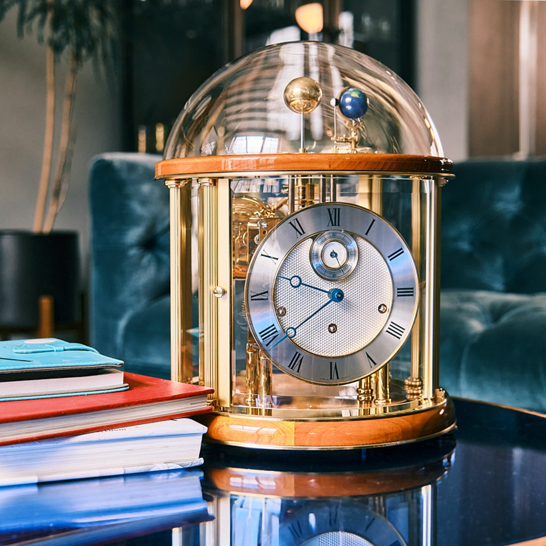 Cherry wood and brass Tellurium clock with glass and visible gears in living room on blue table