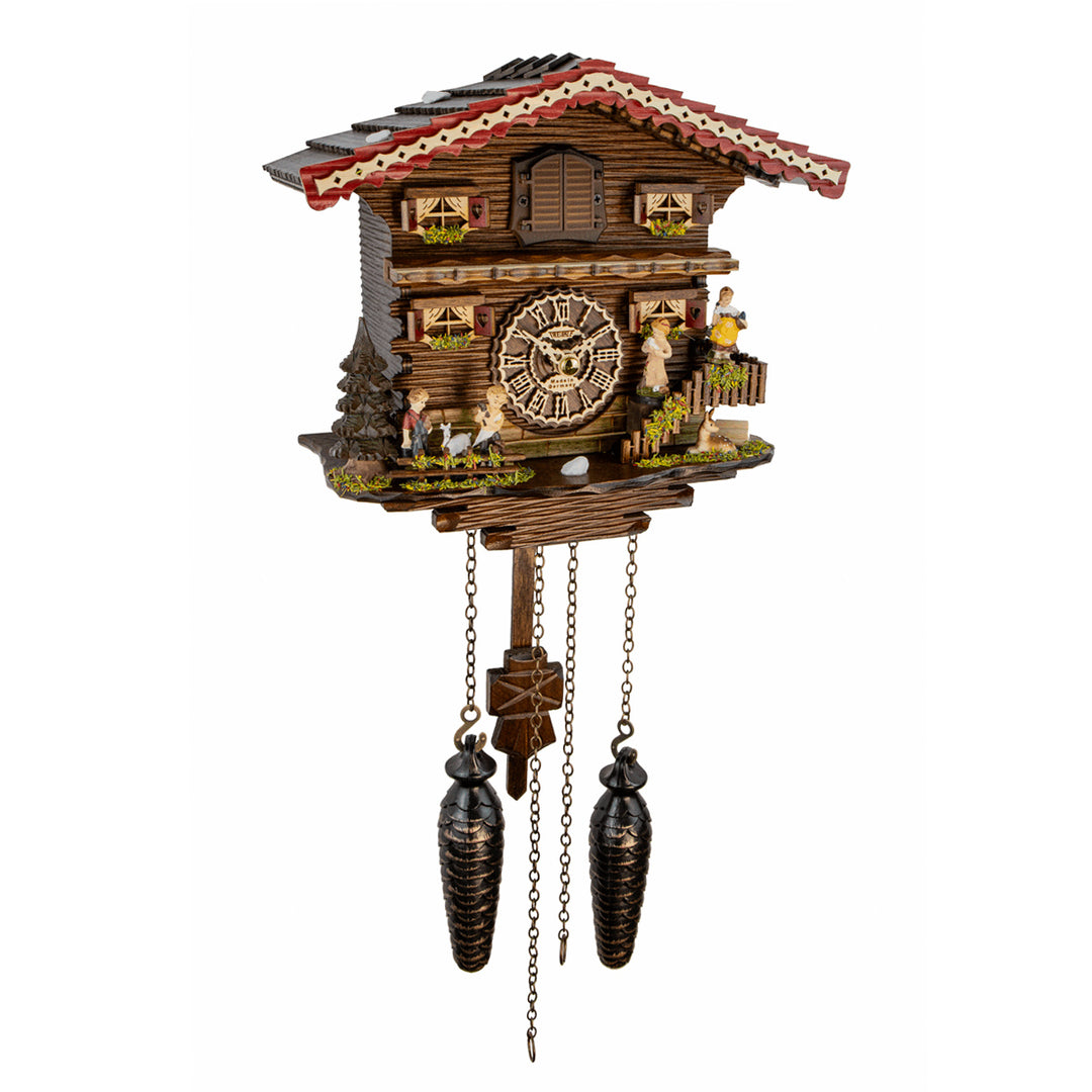 A traditional Black Forest cuckoo clock shaped like a mountain cabin, featuring a detailed clock face, small figurines, and two dark metal pendulums hanging below, shown against a plain white background.